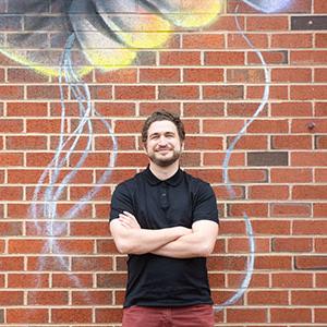 Owen Silverman Andrews leaning against a brick wall covered in art