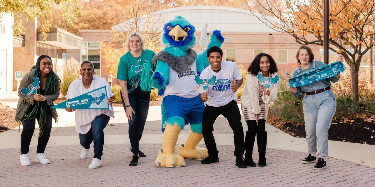 A group of students posing with AACC mascot, Swoop, while holding AACC gear.